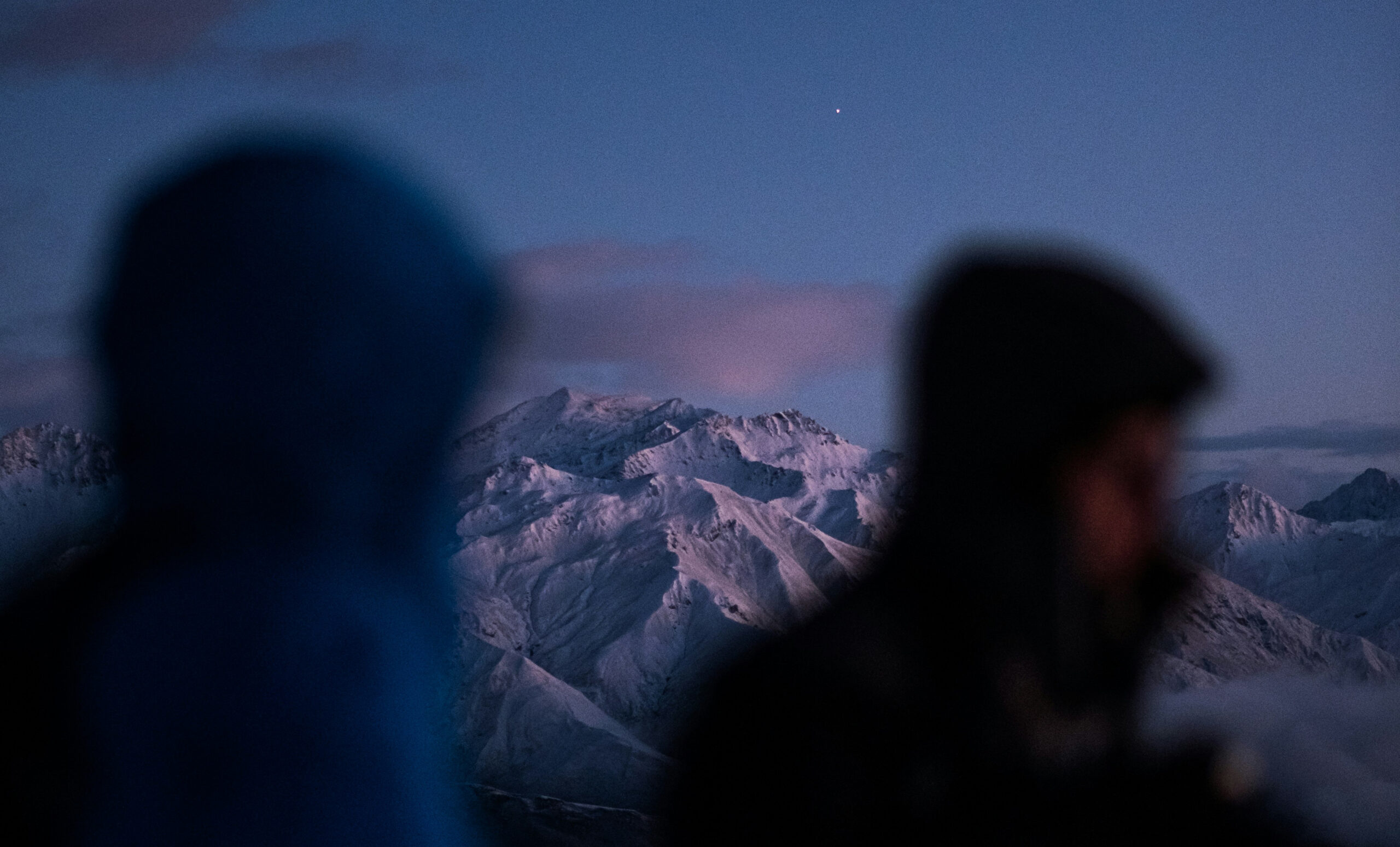 Close up of 2 people with snowy mountains in the background low sunlight